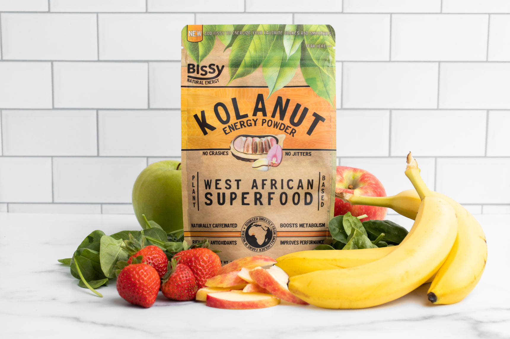 Kolanut Energy Powder by Bissy pictured with fresh fruits and vegetables ready to blend into a smoothie